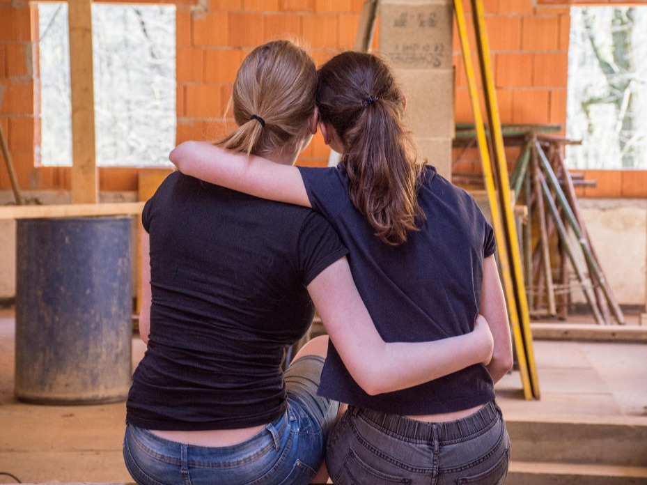Two people, seen from behind, sitting with arms around each other in a partially constructed home.