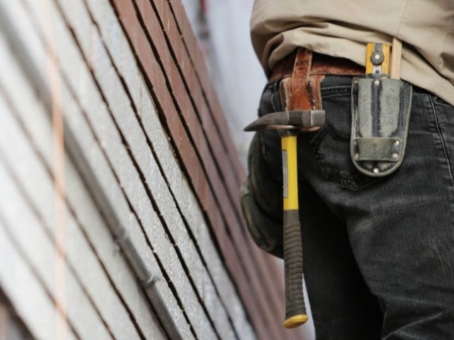 Close-up of a construction worker’s tool belt with a hammer, standing next to a stack of bricks