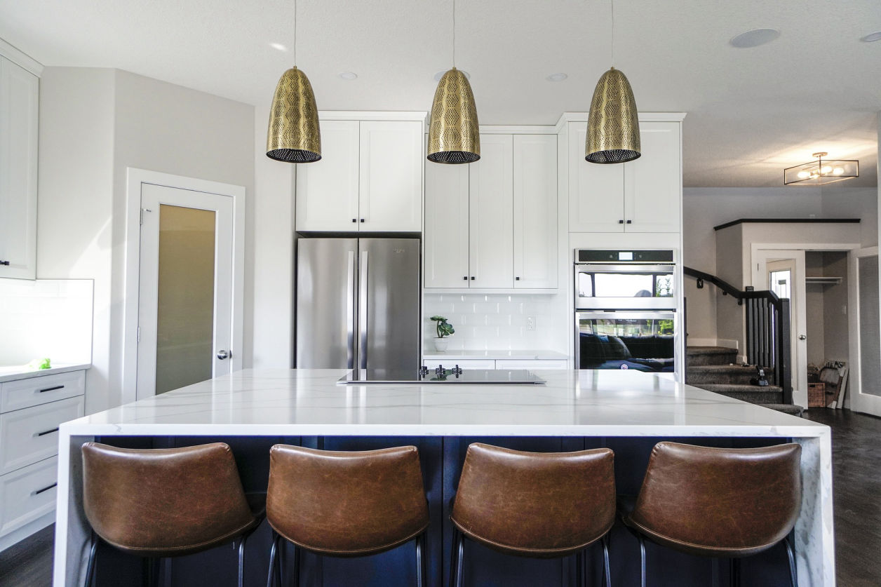 Contemporary white kitchen with a large island, brown barstools, and brass pendant lights.